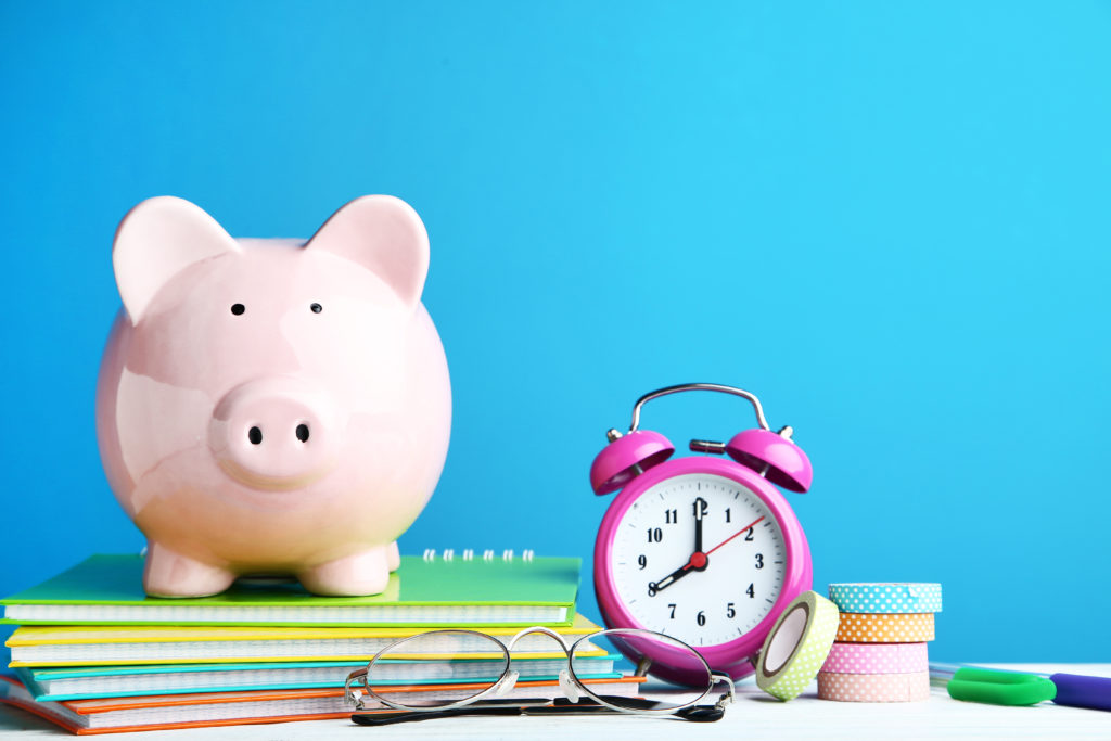 Pink piggy bank with journals, glasses and alarm clock on blue background.